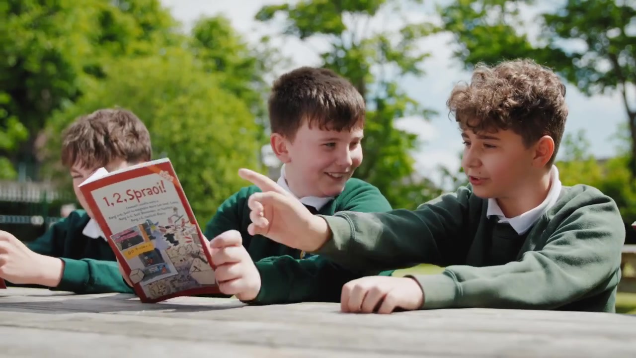 Pupils in green uniforms sharing a book at an outdoor table.