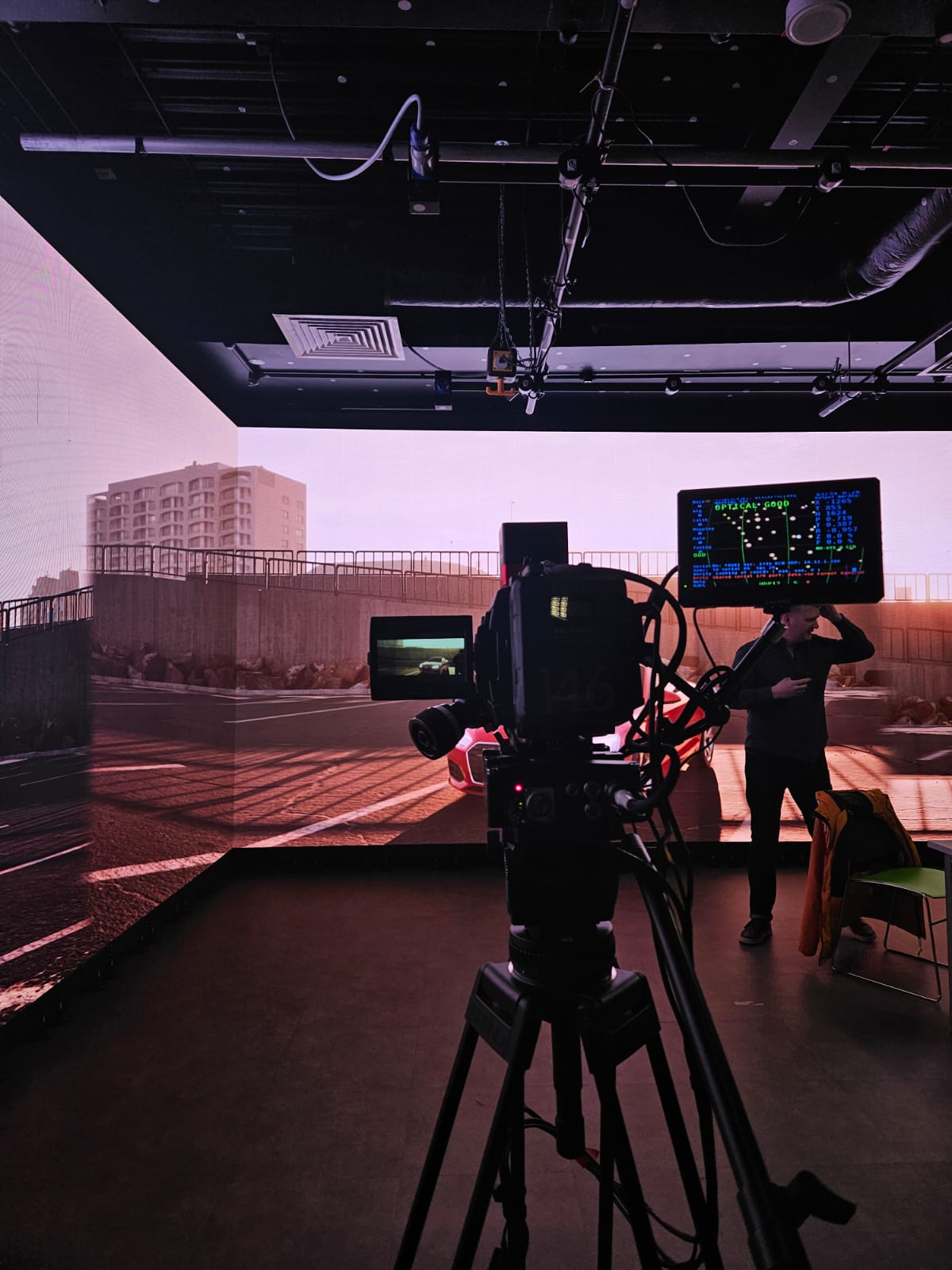 A camera and monitor facing a cityscape backdrop in a darkened studio.