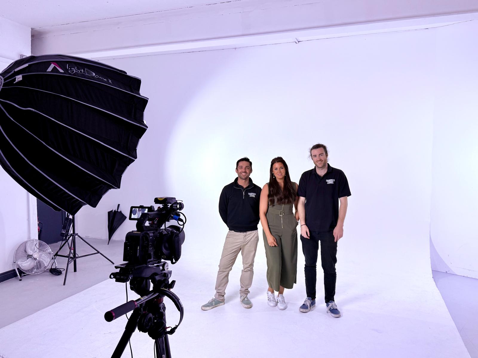 Three members of the SlackPress team beside camera and lighting equipment in a white studio.